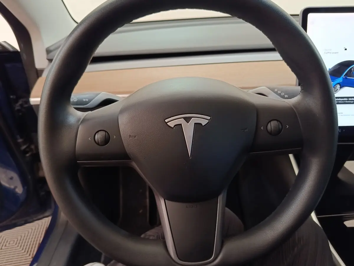 Vue rapprochée du volant noir de la Tesla Model 3 Long Range 2020 avec tableau de bord en bois clair visible.