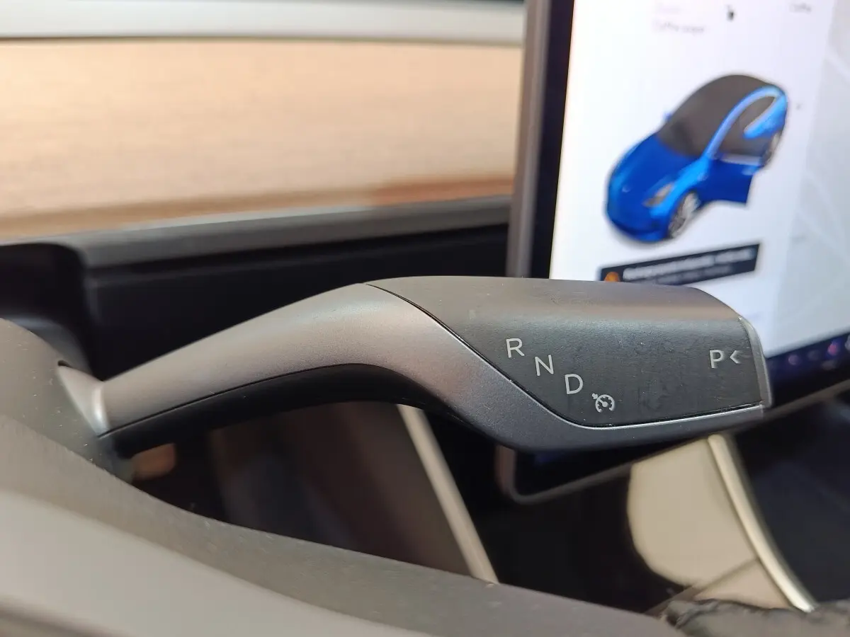 Le levier de vitesses automatique de la Tesla Model 3 Long Range, vue rapprochée à l'intérieur, avec écran tactile en arrière-plan.