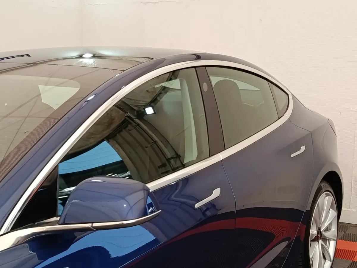 Vue côté gauche rapprochée d’une Tesla Model 3 Long Range bleu, mettant en valeur la ligne fluide et les rétroviseurs électriques.