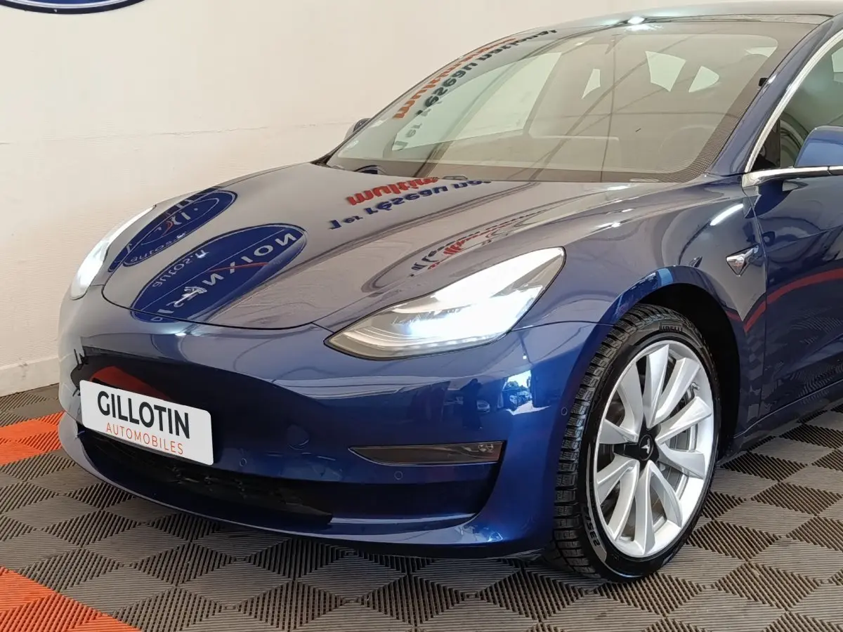 Vue 3/4 avant droite d'une Tesla Model 3 Long Range bleu électrique avec phares LED et jantes argentées.