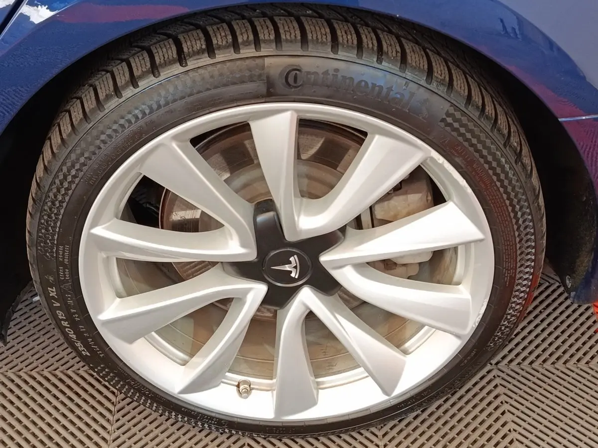 Gros plan sur la jante argentée et le pneu Continental d'une Tesla Model 3 bleu, côté gauche avant.