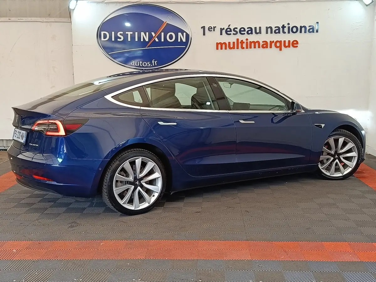 Profil droit d'une Tesla Model 3 Long Range bleu électrique, avec jantes alliage et feux arrière LED distinctifs.