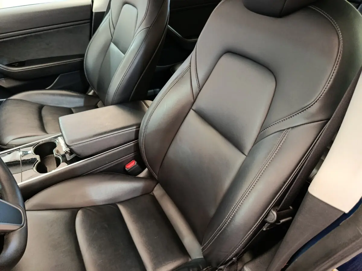 Vue intérieure rapprochée des sièges avant en cuir noir d’une Tesla Model 3 Long Range bleu, avec console centrale visible.