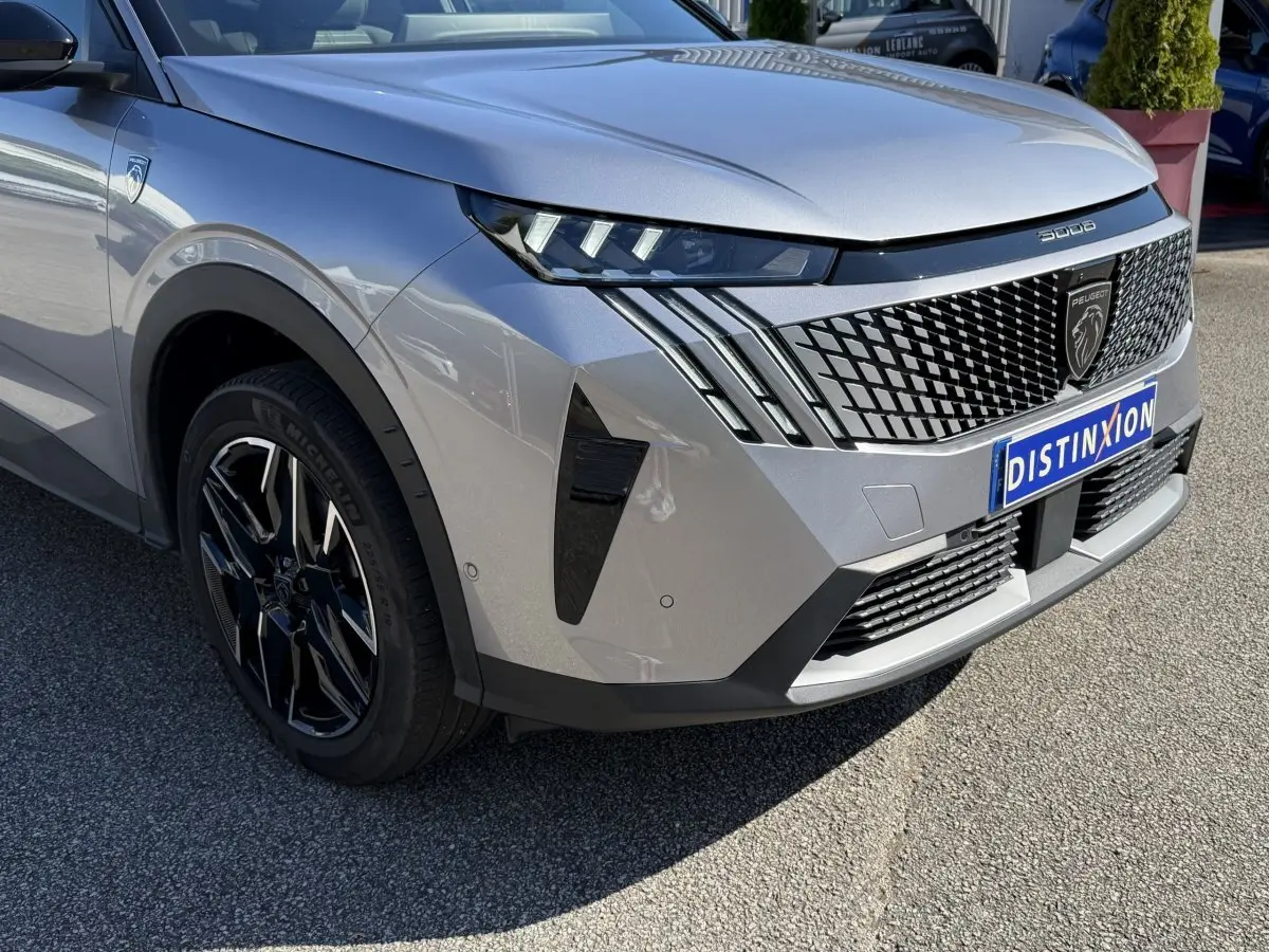 Vue 3/4 avant droit du Peugeot 3008 gris clair avec calandre noire à motif géométrique et phares LED distinctifs.