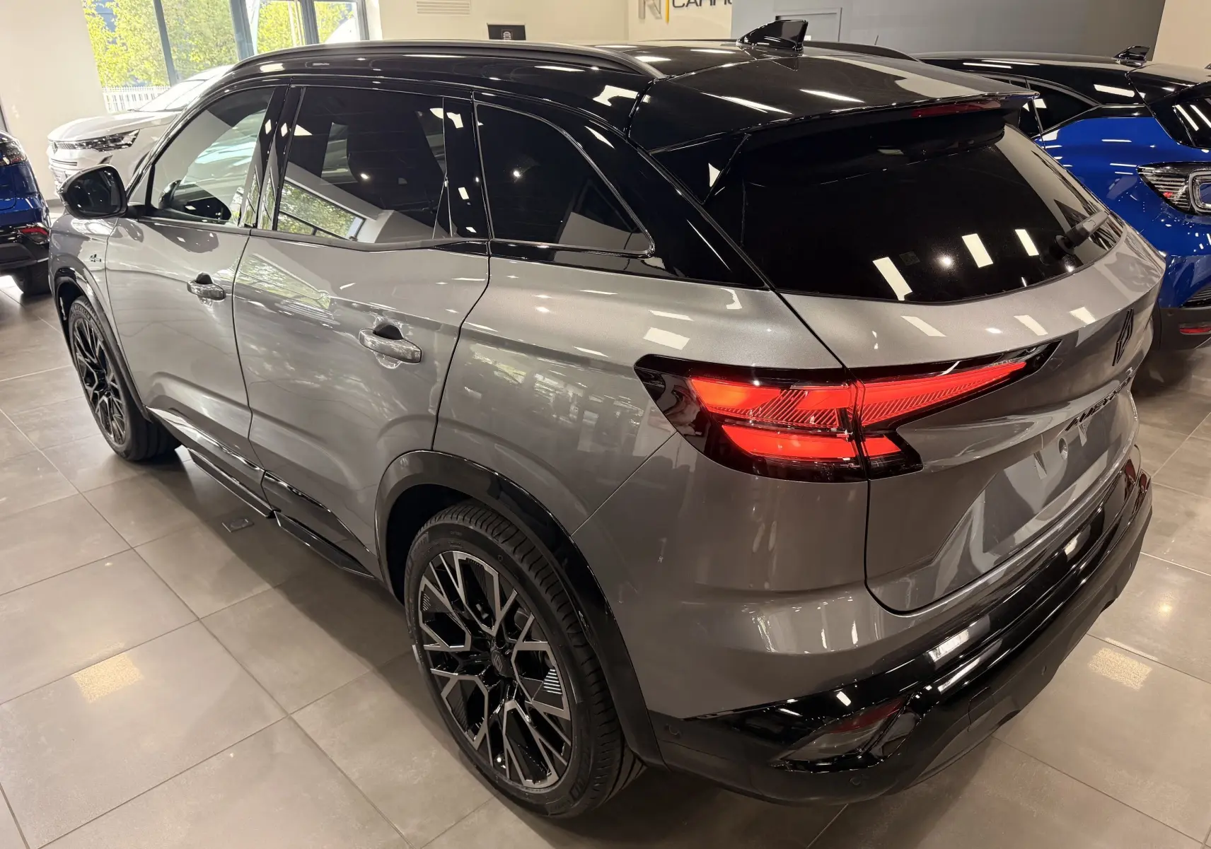 Vue 3/4 arrière droite du Renault Austral gris schiste avec toit noir et feux arrière allumés en intérieur showroom.