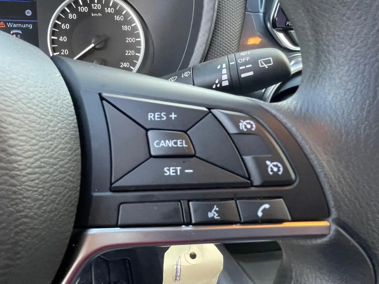 Gros plan sur les commandes noires du régulateur de vitesse au volant cuir du Nissan Juke gris Ceramic 2024