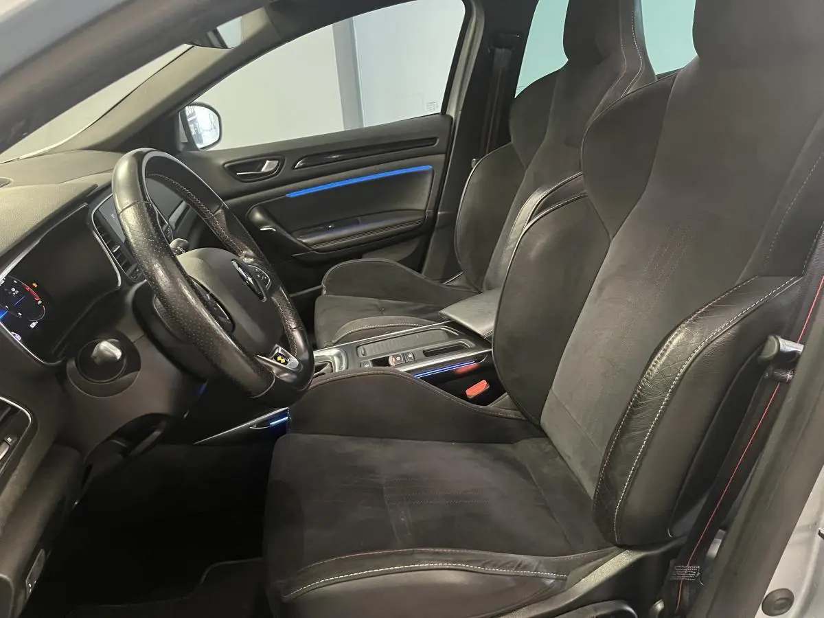 Intérieur avant de la Renault Mégane gris Highland, sièges sport Alcantara noirs avec surpiqûres rouges et éclairage d'ambiance bleu.