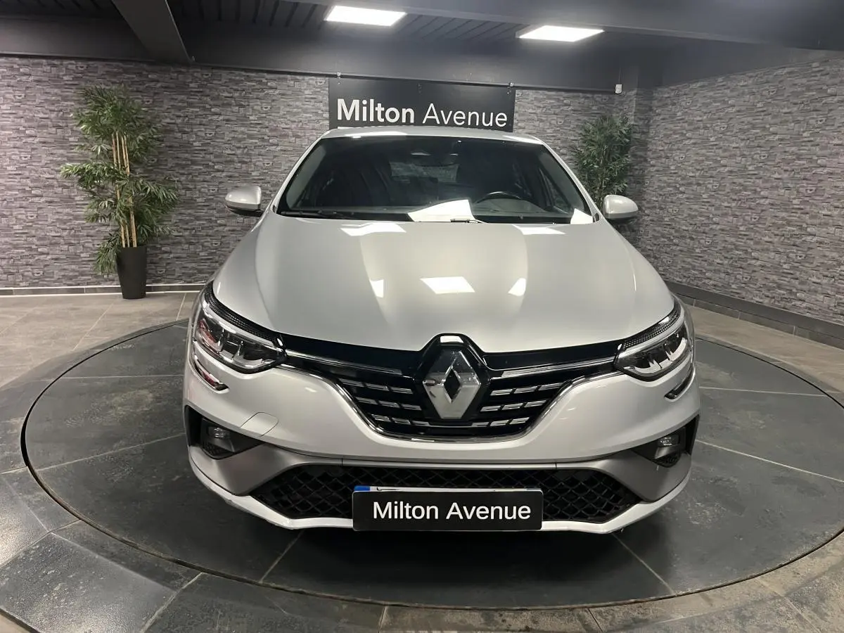 Vue frontale d'une Renault Mégane gris Highland avec calandre noire et logo chromé, en showroom intérieur.