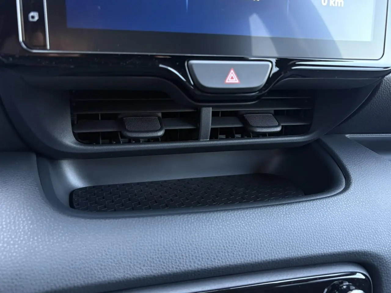 Gros plan sur la console centrale noire de la Toyota Yaris hybride 2025, avec les aérateurs et le bouton de warning visible.