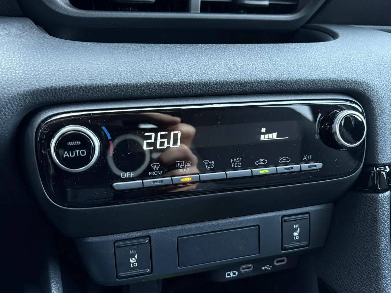 Gros plan sur la console centrale noire de la Toyota Yaris hybride 2025, affichant la climatisation à 26°C et les sièges chauffants activés.