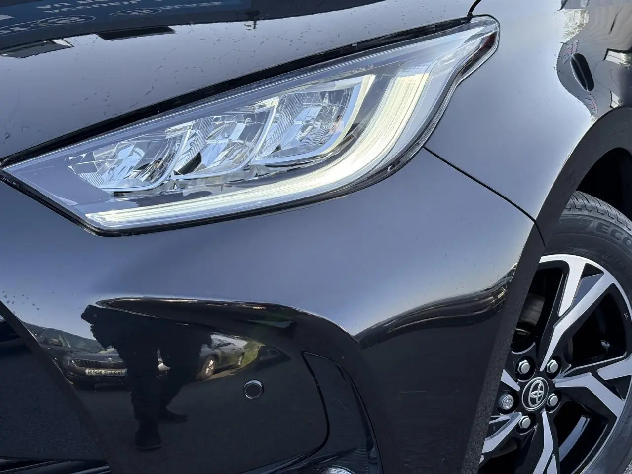 Gros plan sur le phare avant droit et la jante alliage 16'' d'une Toyota Yaris Hybride 2025 noir intense.
