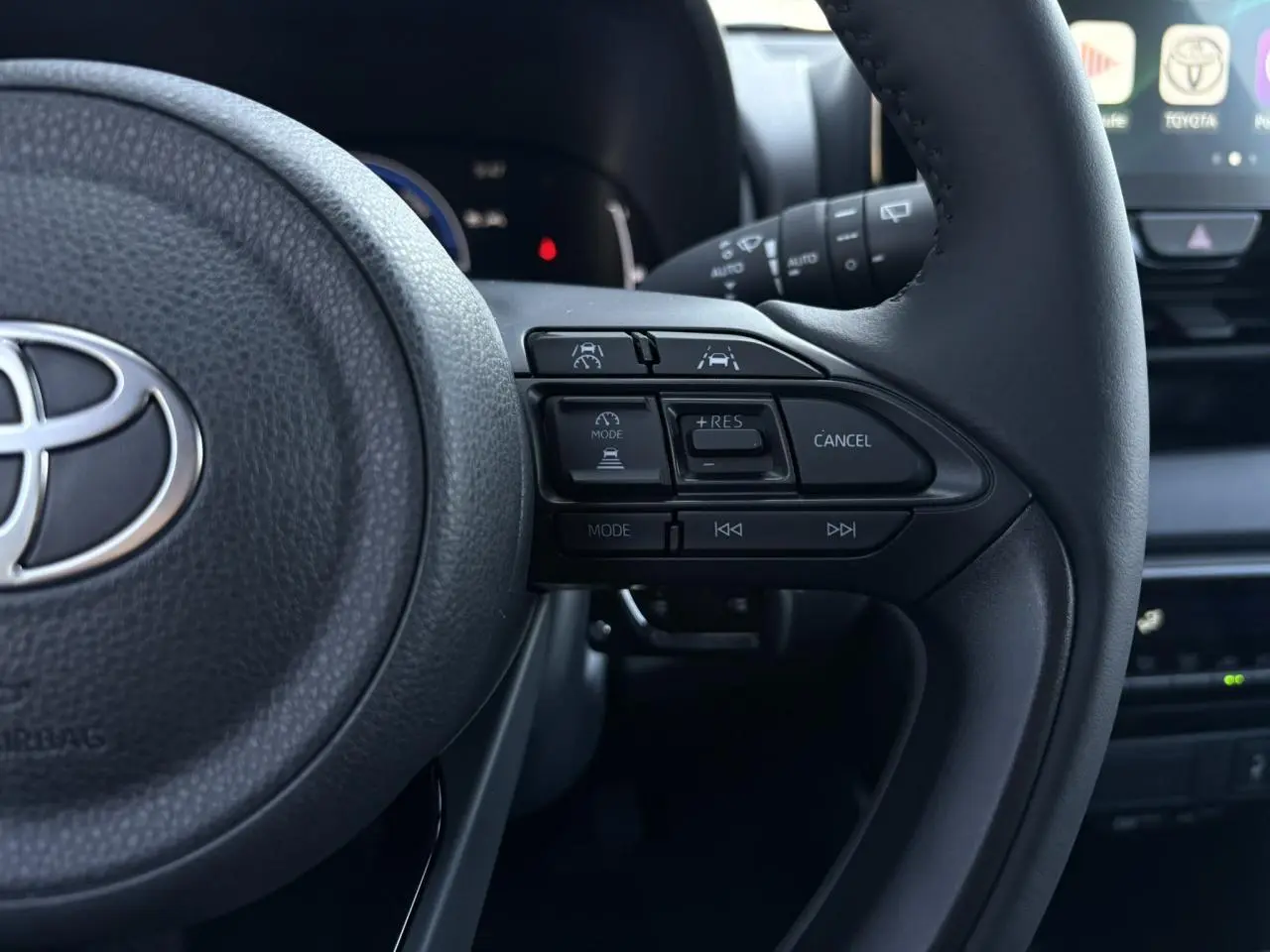 Gros plan sur le volant cuir noir de la Toyota Yaris 2025 hybride, montrant les commandes de régulateur adaptatif côté droit.