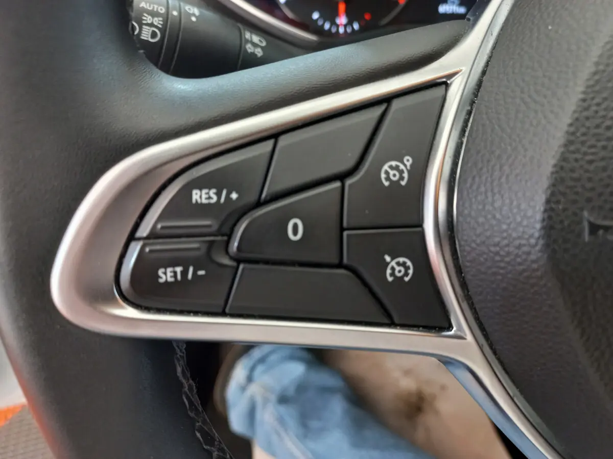 Gros plan sur les commandes de régulateur de vitesse au volant cuir noir de la Renault Clio Business blanche de 2021.