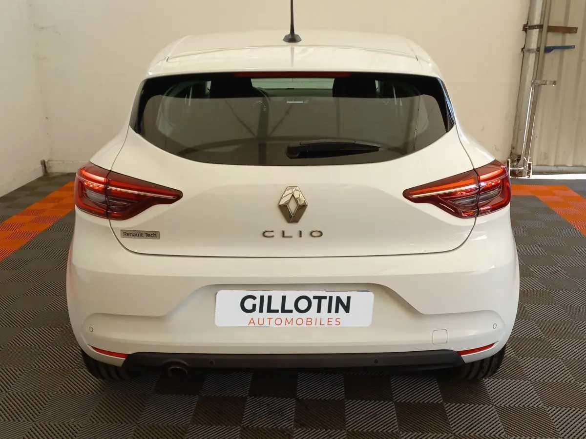 Vue arrière d'une Renault Clio blanche 2021 avec feux LED et logo centré sur un sol damier noir et orange.