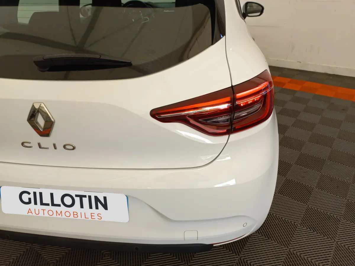 Vue arrière droite d'une Renault Clio Business blanche avec feux arrière LED et logo visible sur un sol à damiers.