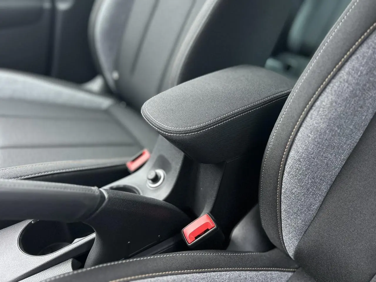 Gros plan sur l'accoudoir central et les sièges tissu gris du Skoda Kamiq TSI 116 DSG7, intérieur moderne et fonctionnel.