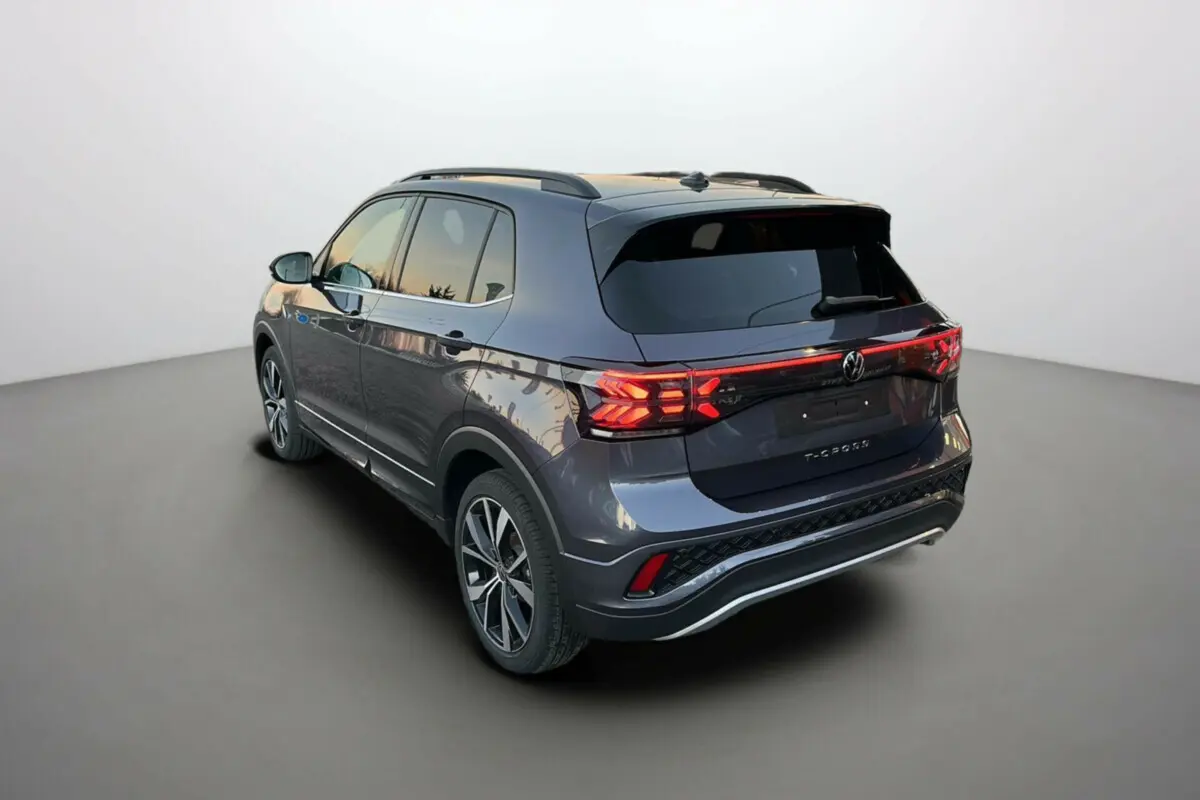 Volkswagen T-Cross TSI 116 DSG7 R-Line gris cendré, vue 3/4 arrière droit avec feux arrière allumés et jantes 18 pouces.