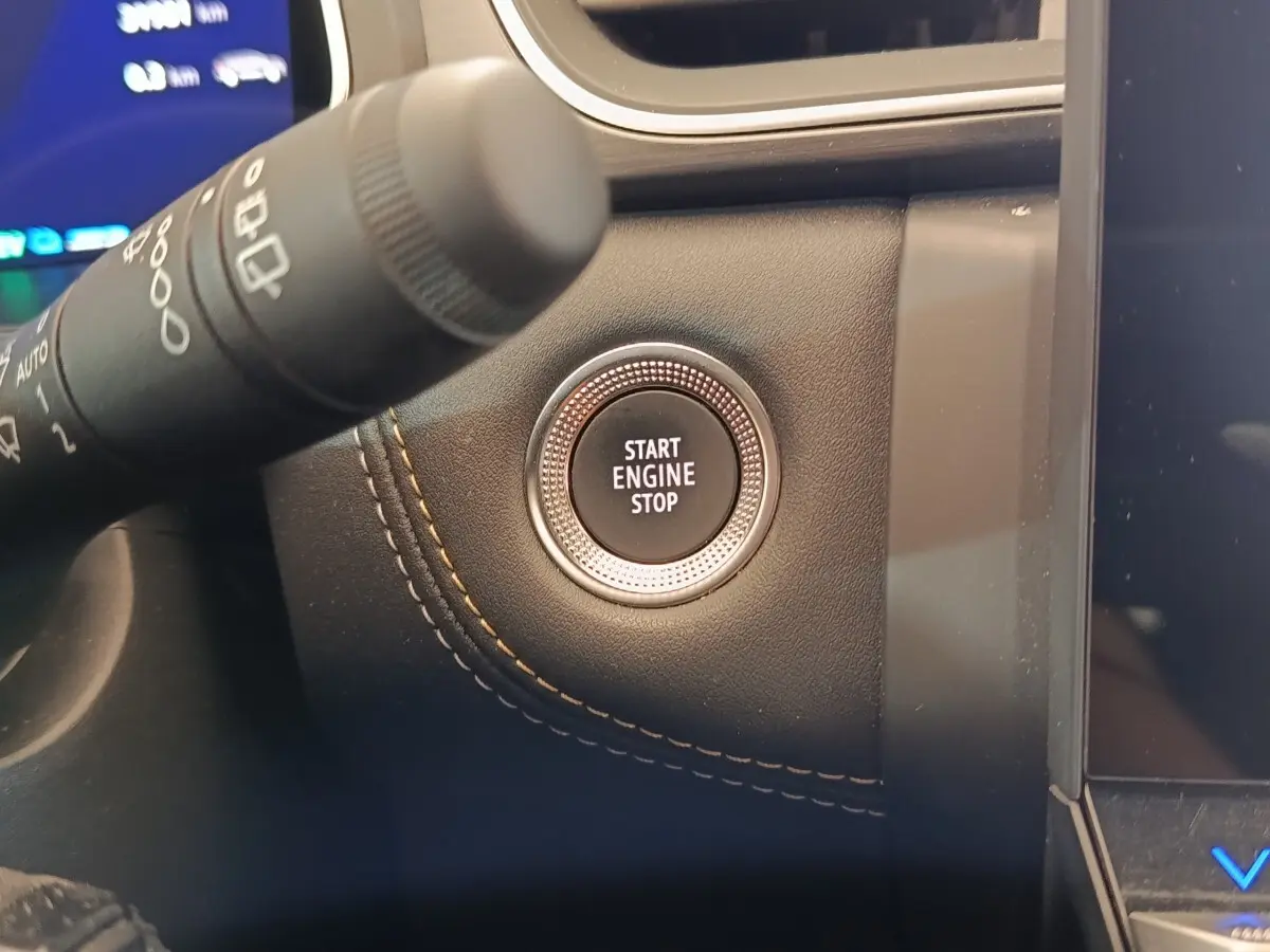 Gros plan sur le bouton Start Engine Stop entouré de cuir noir avec surpiqûres orange dans le tableau de bord Renault Symbioz.