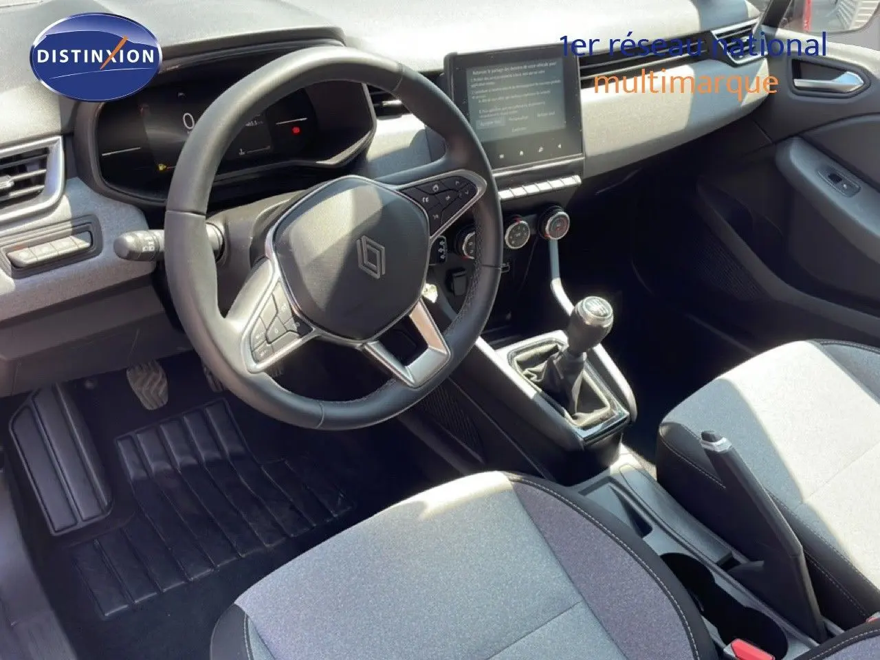 Vue intérieure de face du poste de conduite d'une Renault Clio 2025, volant cuir multifonction et levier de vitesse manuel visibles.