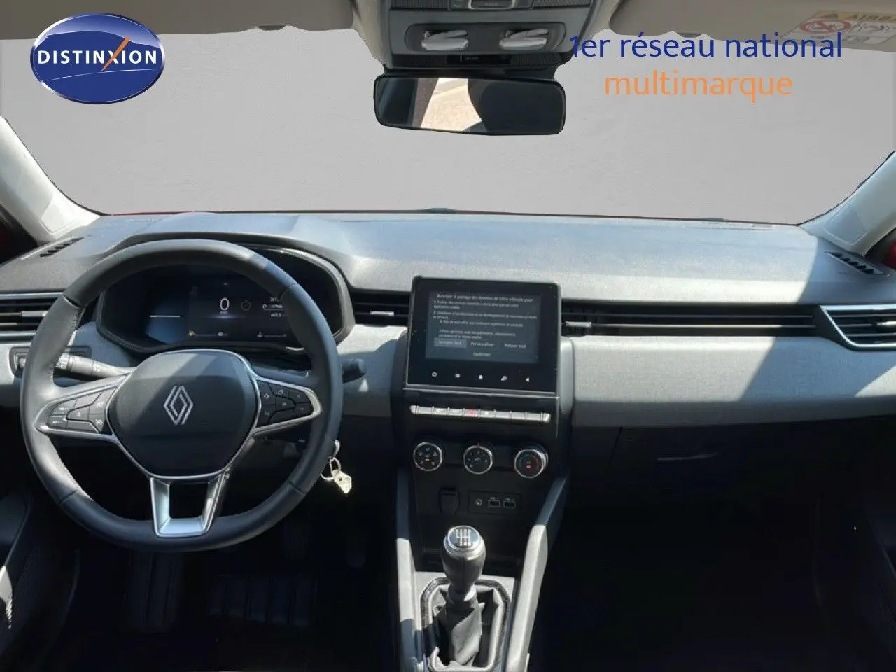 Vue intérieure avant du tableau de bord de la Renault Clio rouge flamme, avec volant cuir et écran tactile central.