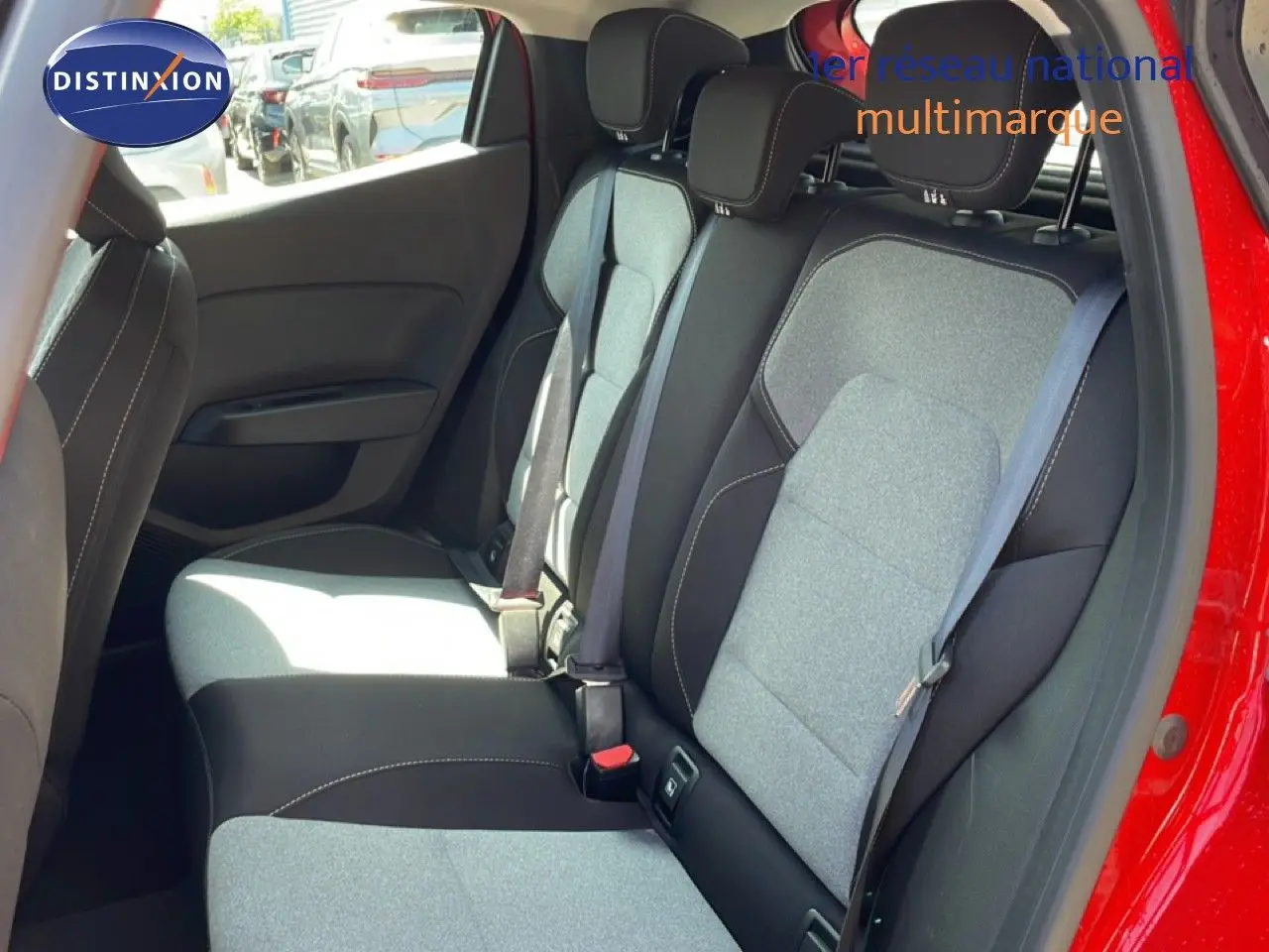 Vue intérieure de la banquette arrière d'une Renault Clio rouge flamme métal, sièges tissu gris et noir avec ceintures visibles.