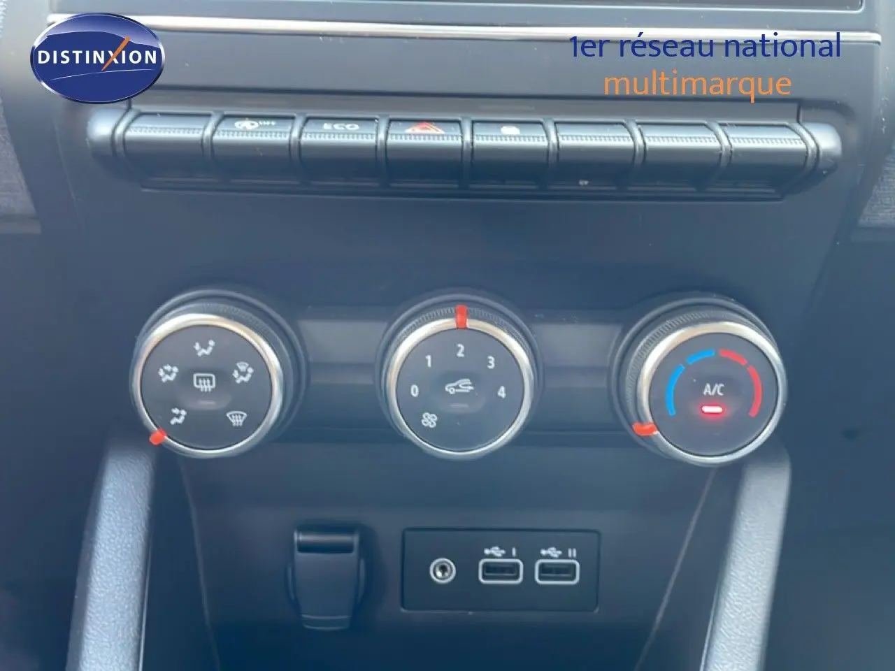 Gros plan sur les commandes de climatisation et ventilation de la Renault Clio rouge flamme, avec boutons rotatifs et ports USB.