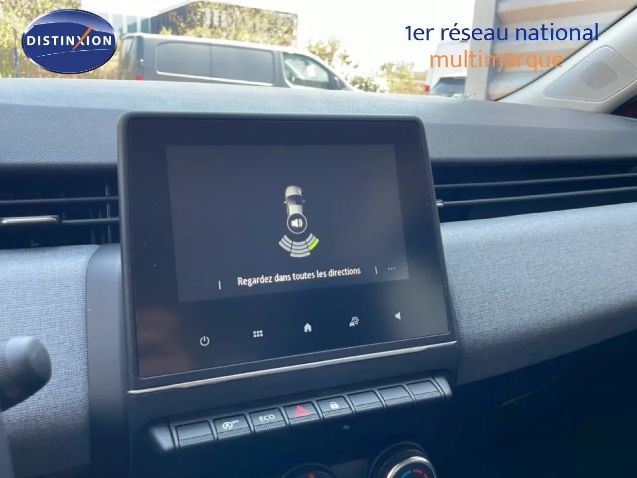 Vue intérieure du tableau de bord de la Renault Clio rouge flamme, avec écran tactile central et commandes climatisation visibles.
