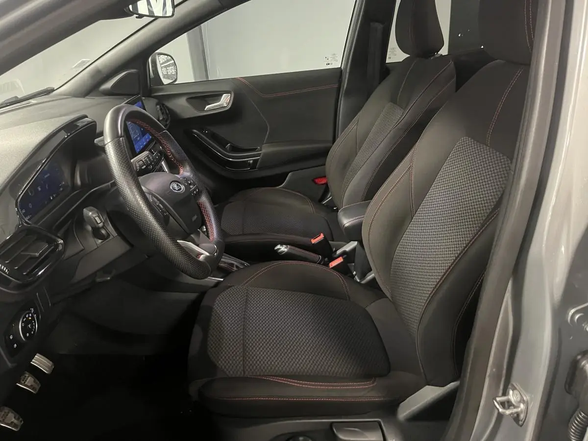 Intérieur avant droit du Ford Puma gris, sièges tissu noir avec surpiqûres rouges et volant ST-Line à méplat.