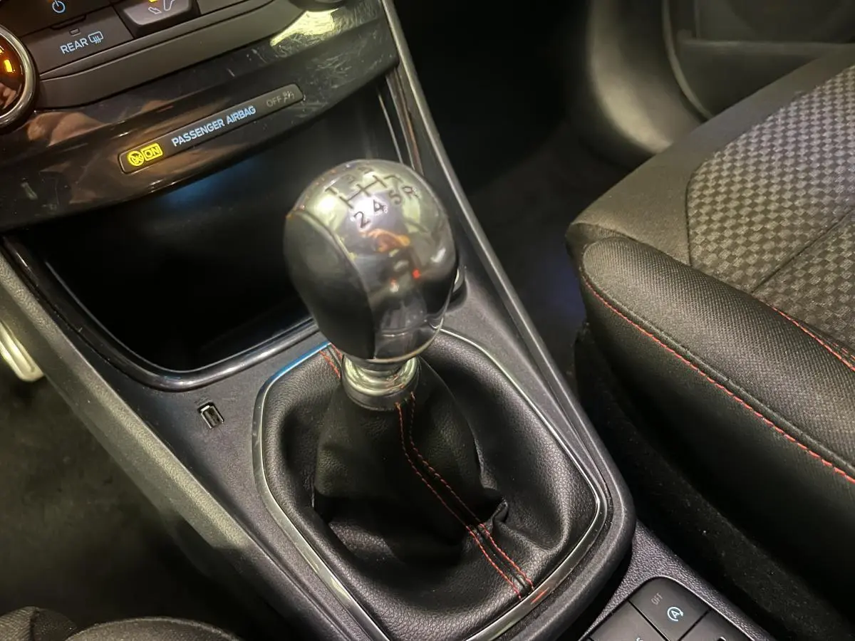 Levier de vitesses manuel gainé de cuir noir avec surpiqûres rouges dans l'habitacle du Ford Puma gris.