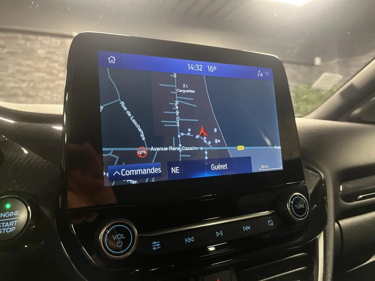 Écran tactile central du Ford Puma gris, affichant la navigation GPS avec commandes audio et bouton démarrage visible.