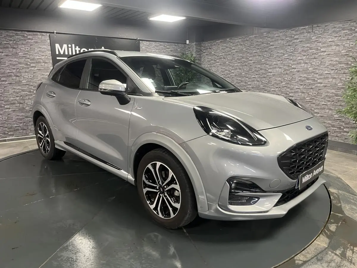 Ford Puma gris métallisé en 3/4 avant droit avec jantes alliage noires et barres de toit noires visibles