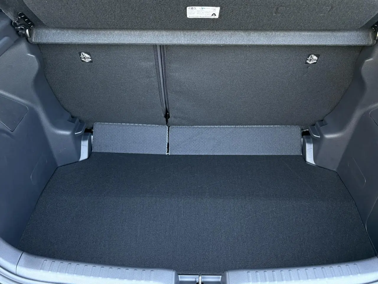 Coffre ouvert de la Toyota Yaris Hybride 2025 en noir intense, montrant l'espace de chargement vide et les dossiers arrière rabattus.