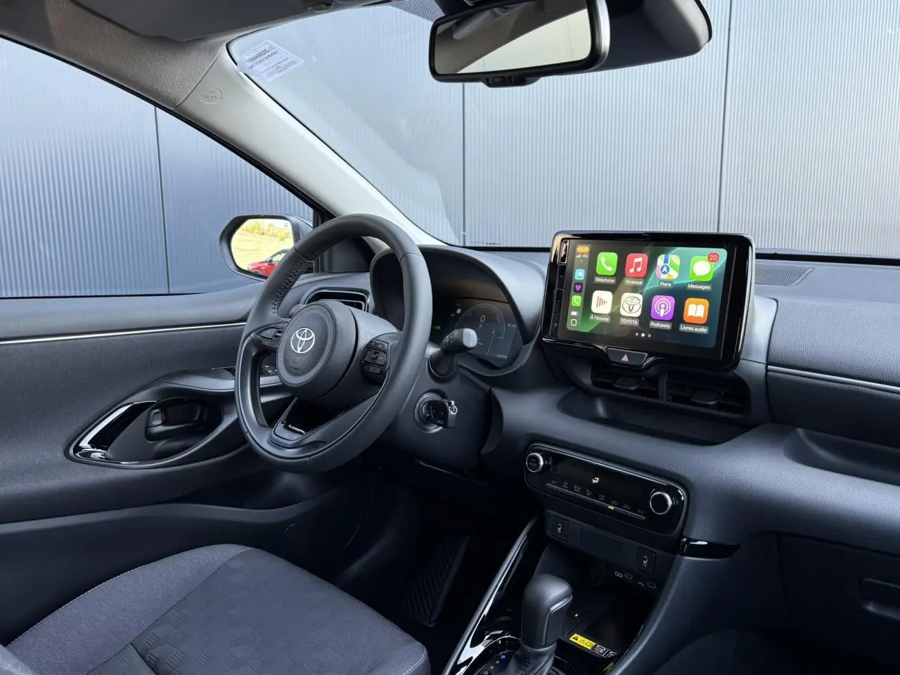 Intérieur avant gauche de la Toyota Yaris Hybride 2025 avec volant cuir, écran tactile et sellerie noire.