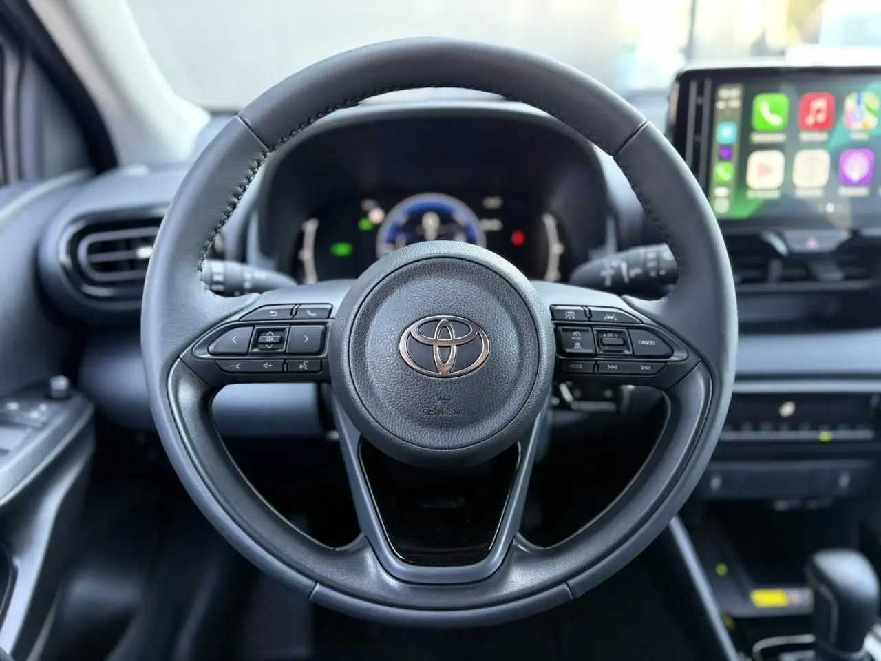 Volant cuir noir de la Toyota Yaris Hybride 2025 vu de face avec commandes intégrées et écran multimédia en arrière-plan.