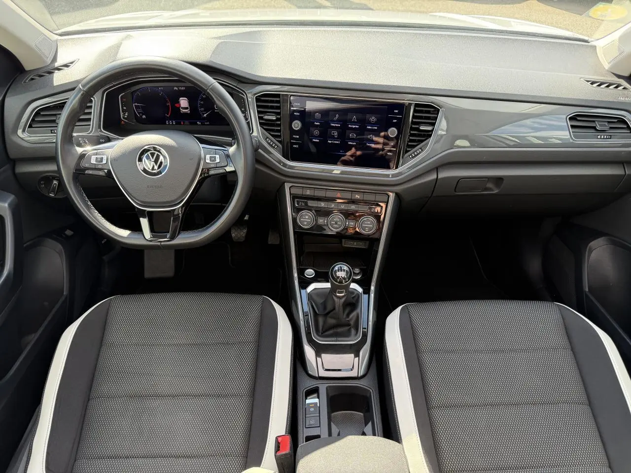 Vue intérieure avant du Volkswagen T-Roc blanc 2022, tableau de bord moderne avec écran tactile et volant multifonction cuir.