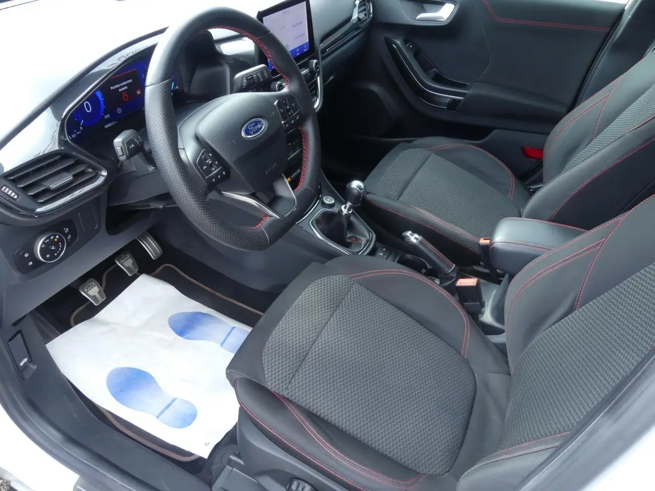Intérieur avant du Ford Puma blanc 2020, sièges tissu noir avec surpiqûres rouges et volant ST-Line à méplat.
