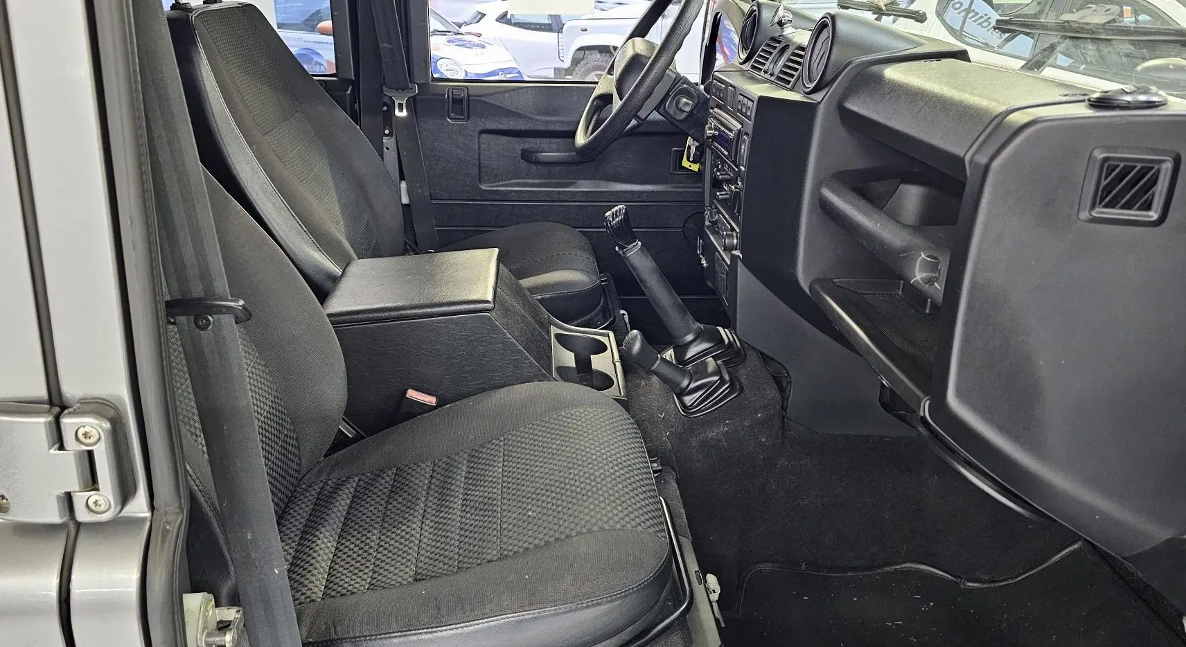 Intérieur du Land Rover Defender 110 Station Wagon gris, vue côté gauche sur les sièges avant et la boîte manuelle.
