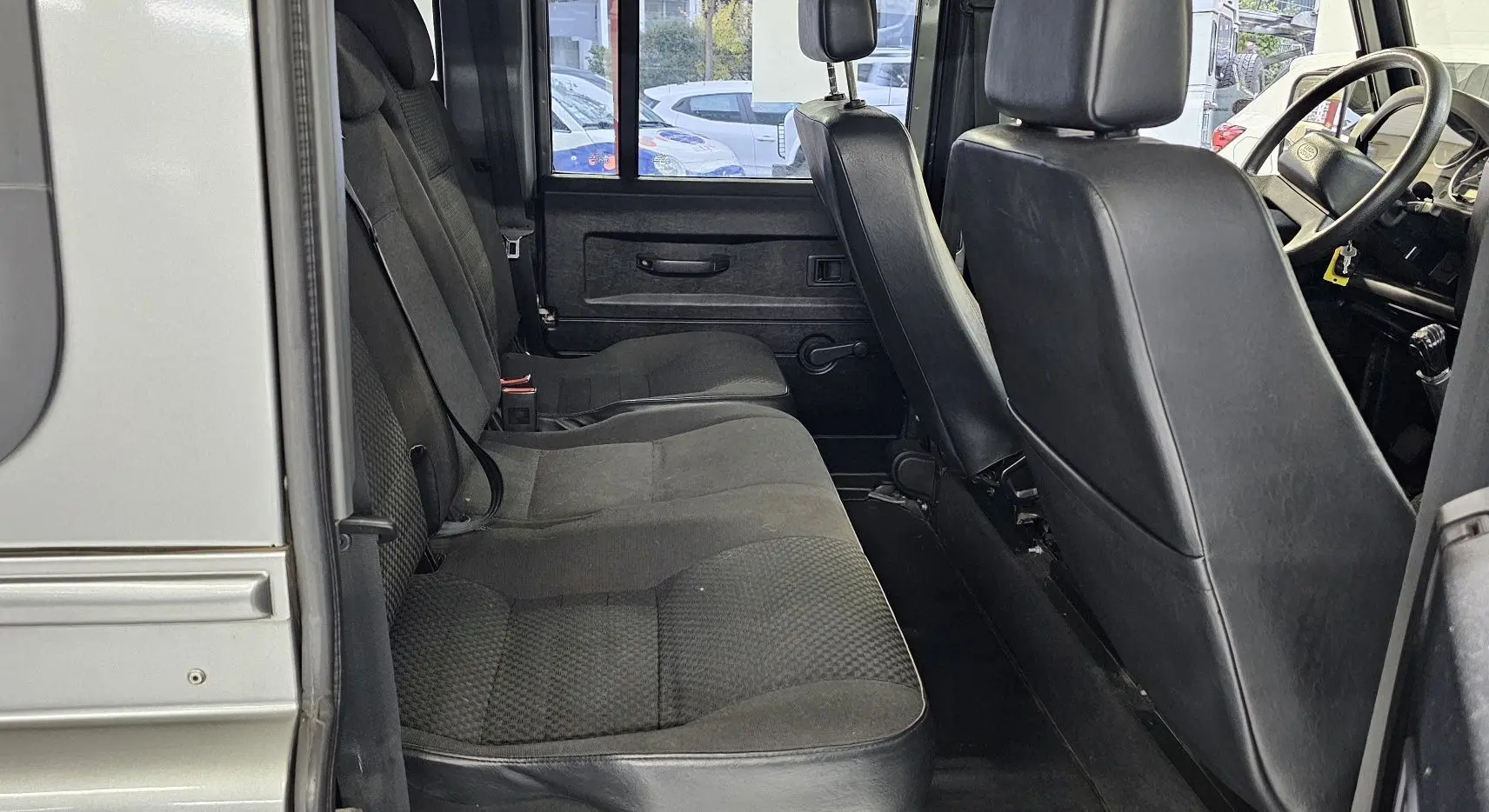 Vue intérieure côté gauche du Land Rover Defender 110 Station Wagon gris, montrant les sièges arrière et avant en tissu et cuir noir.