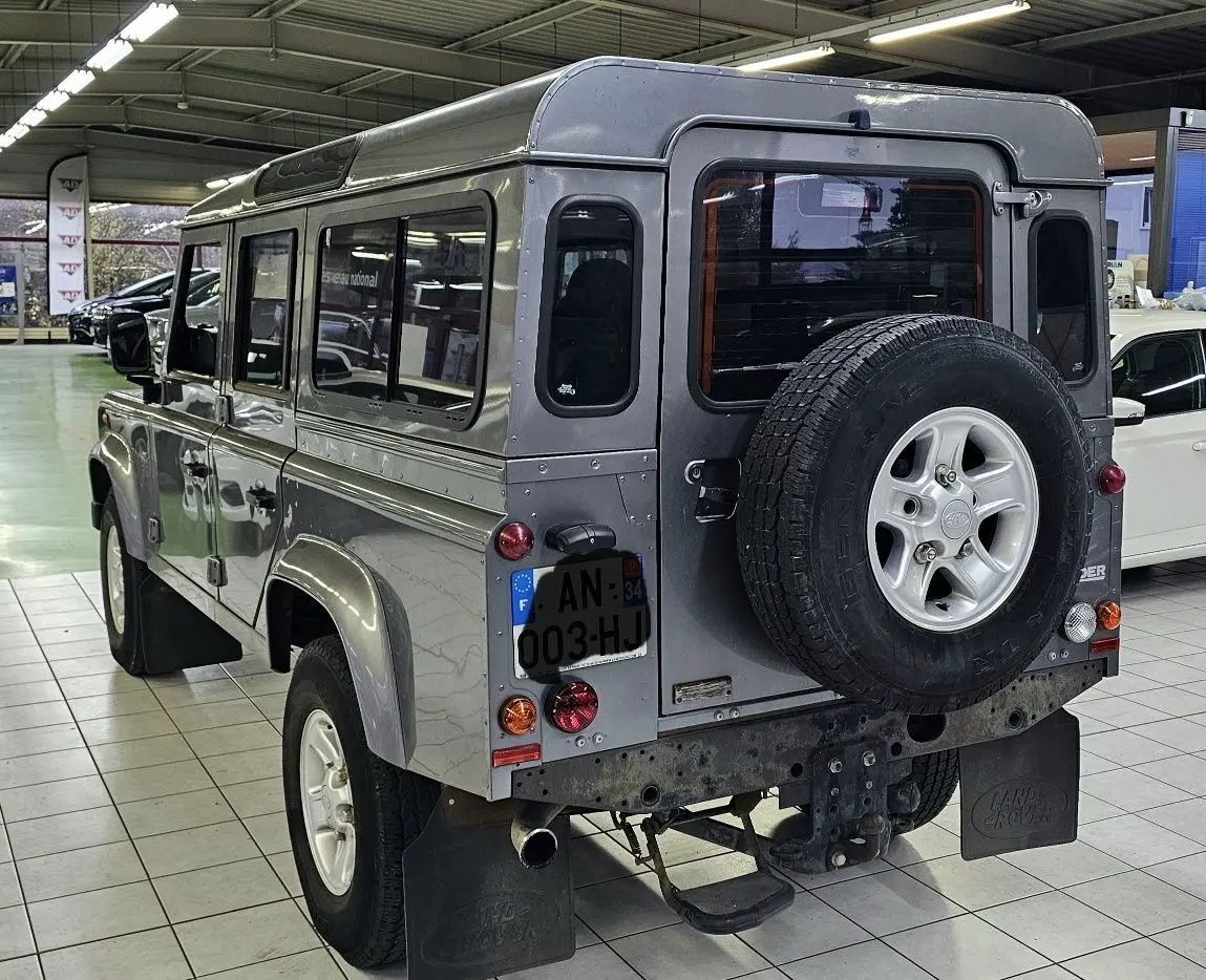 Vue 3/4 arrière droite d'un Land Rover Defender 110 Station Wagon gris avec roue de secours fixée à la porte arrière.