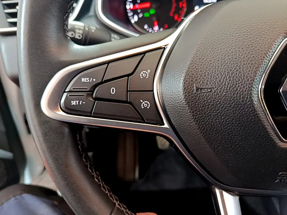 Gros plan sur la partie gauche du volant cuir noir de la Renault Clio Business blanche, avec commandes de régulateur de vitesse.