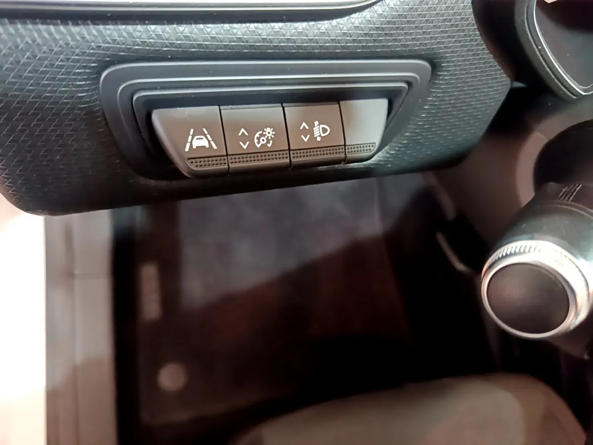 Gros plan sur les commandes de réglage d'assistance et phares dans l'habitacle noir de la Renault Clio Business blanche 2021.