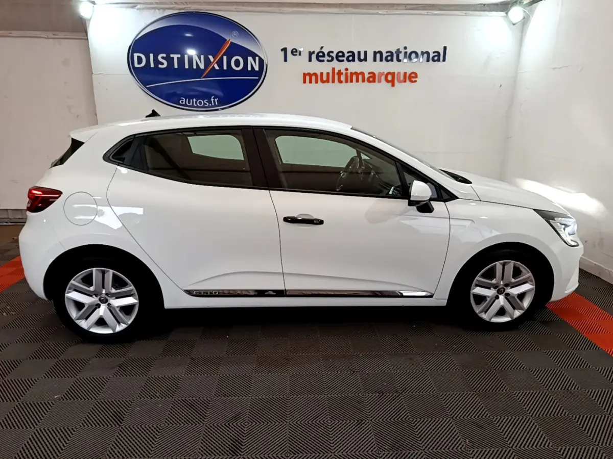 Profil droit d'une Renault Clio Business blanche 2021 avec jantes alliage et poignées noires dans un showroom.