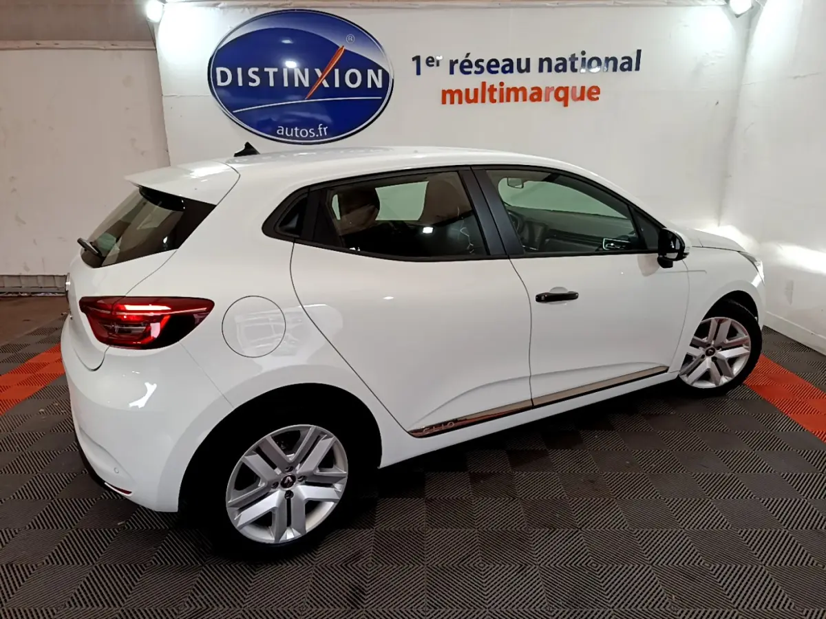 Vue côté droit arrière d'une Renault Clio Business blanche avec feux arrière allumés dans un showroom.
