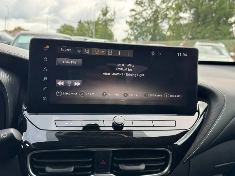 Écran tactile central du tableau de bord du Nissan Juke 2025 affichant une radio FM, ambiance intérieure moderne.