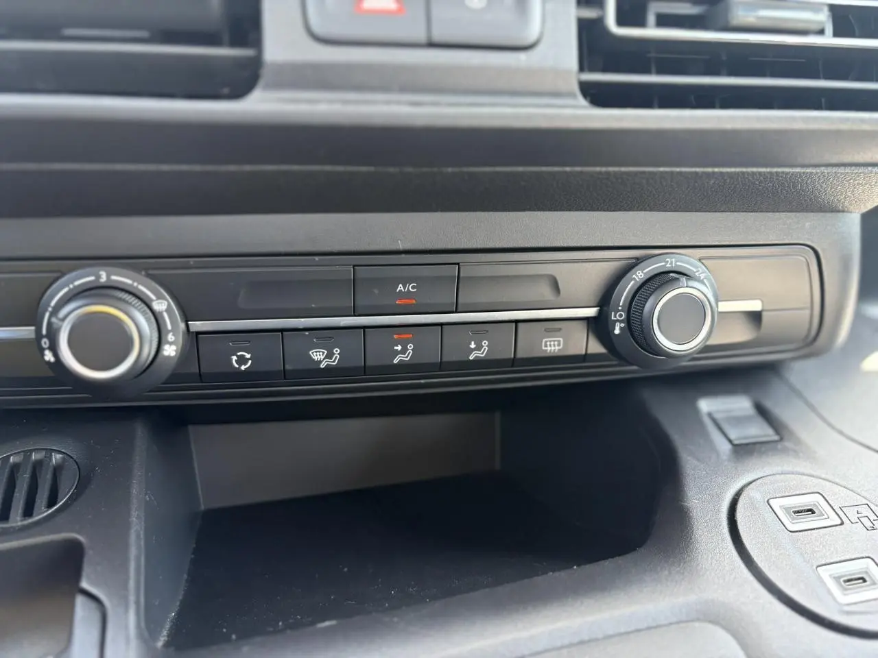 Gros plan sur la console centrale noire du Citroën Berlingo ë-136 avec commandes de climatisation et prises USB visibles.