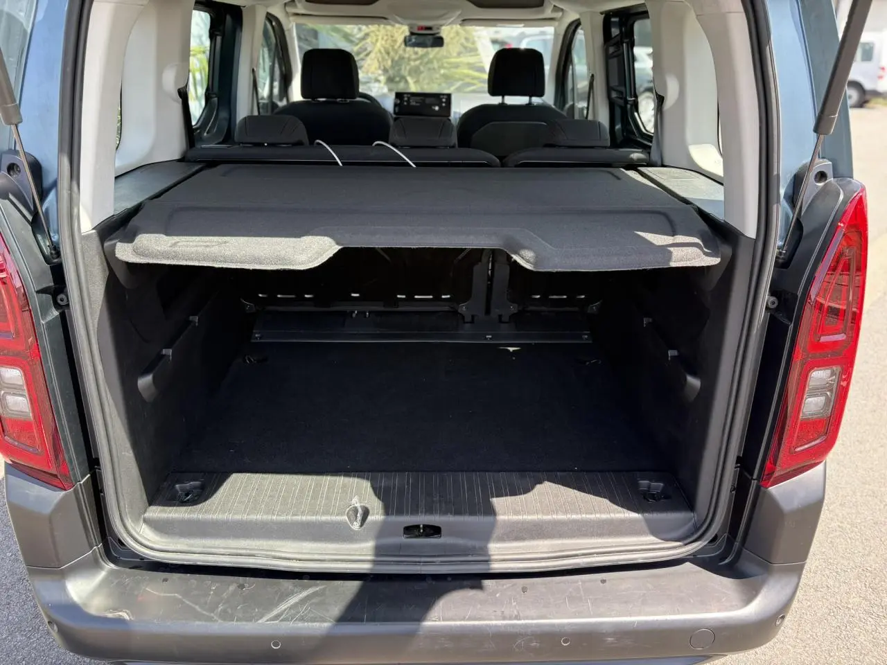 Coffre ouvert vu de l'arrière d'un Citroën Berlingo ë-136 bleu Kiama avec cache-bagages déployé.