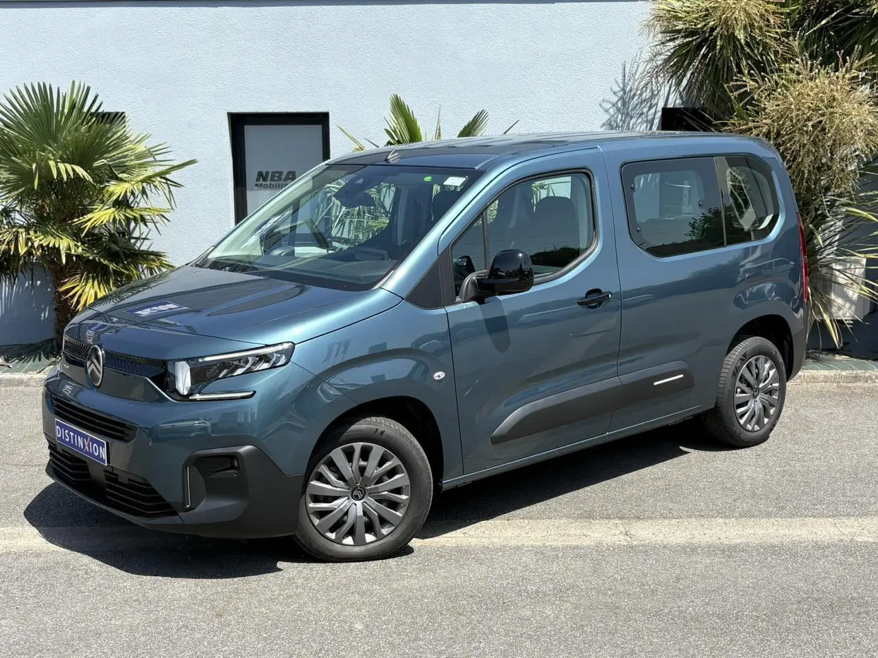 Vue 3/4 avant droite du Citroën Berlingo ë-136 bleu Kiama avec jantes tôles et vitres latérales teintées.