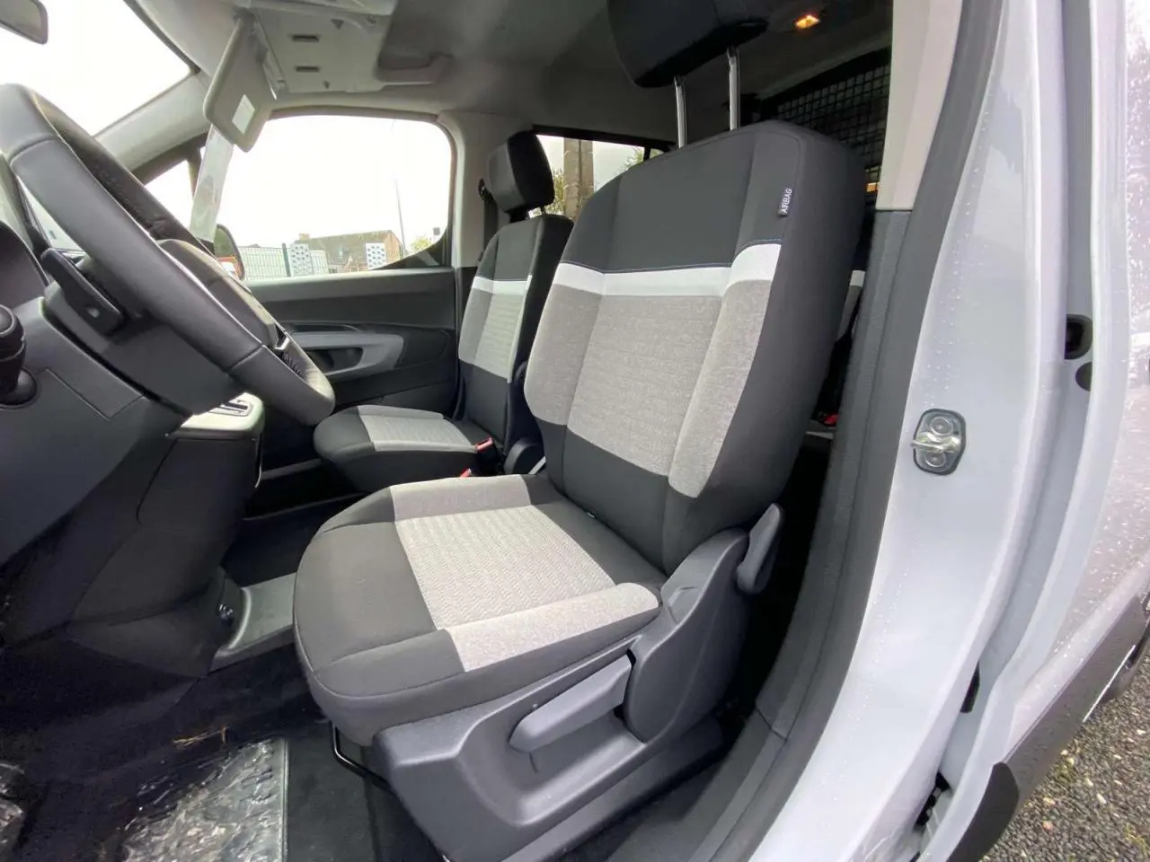 Vue intérieure côté conducteur du Citroën Berlingo Multispace blanc 2025, montrant les sièges avant bi-ton gris et noir.