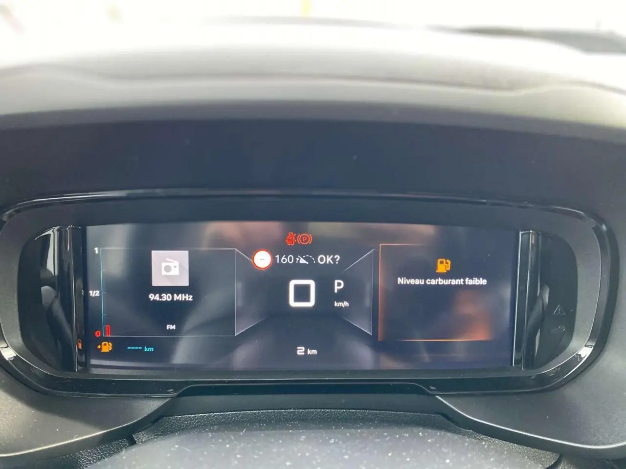 Tableau de bord numérique du Citroën Berlingo 2025 affichant la vitesse à 0 km/h et un avertissement de niveau carburant faible.