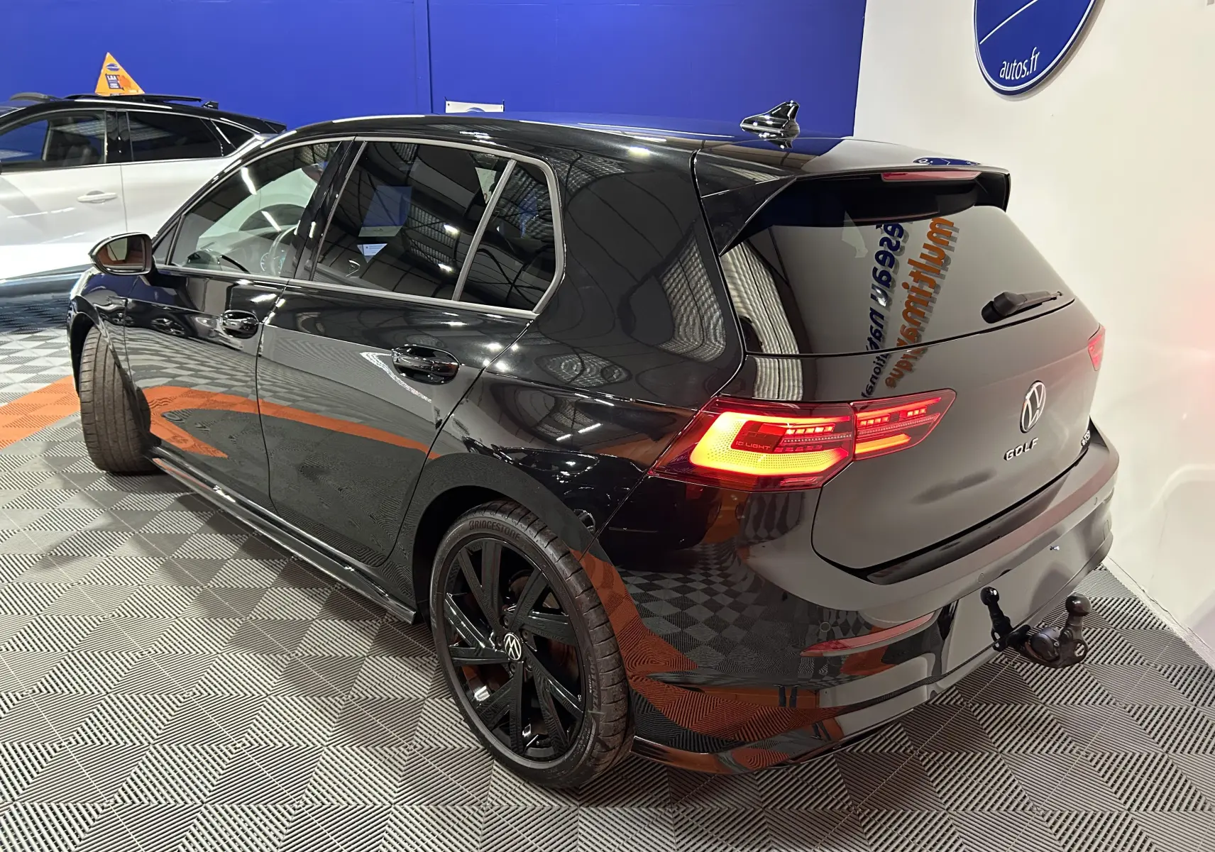 Volkswagen Golf VIII eTSI noire métal vue 3/4 arrière droit avec feux allumés et attelage visible.